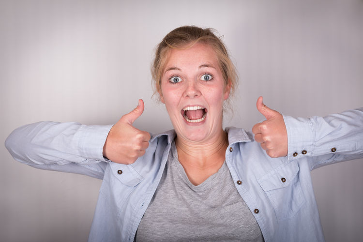 Close-up portrait of happy woman gesturing thumbs up against gray background