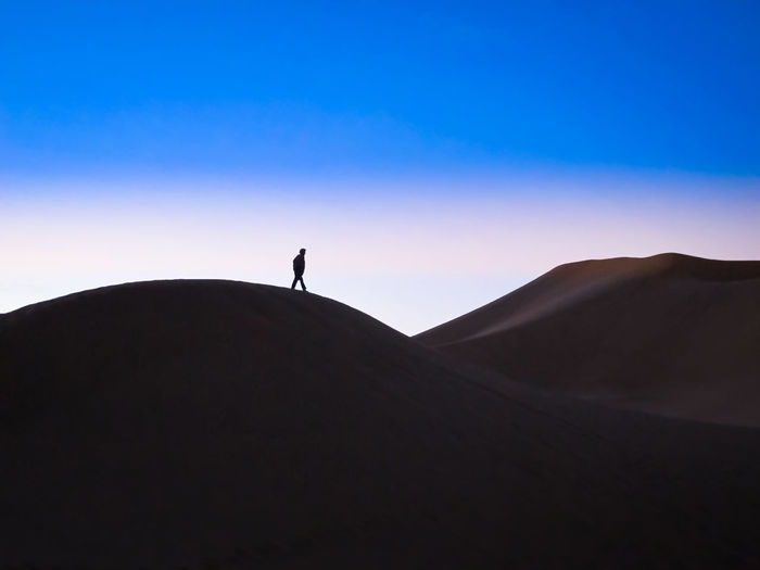 Silhouette person on desert against sky during sunset