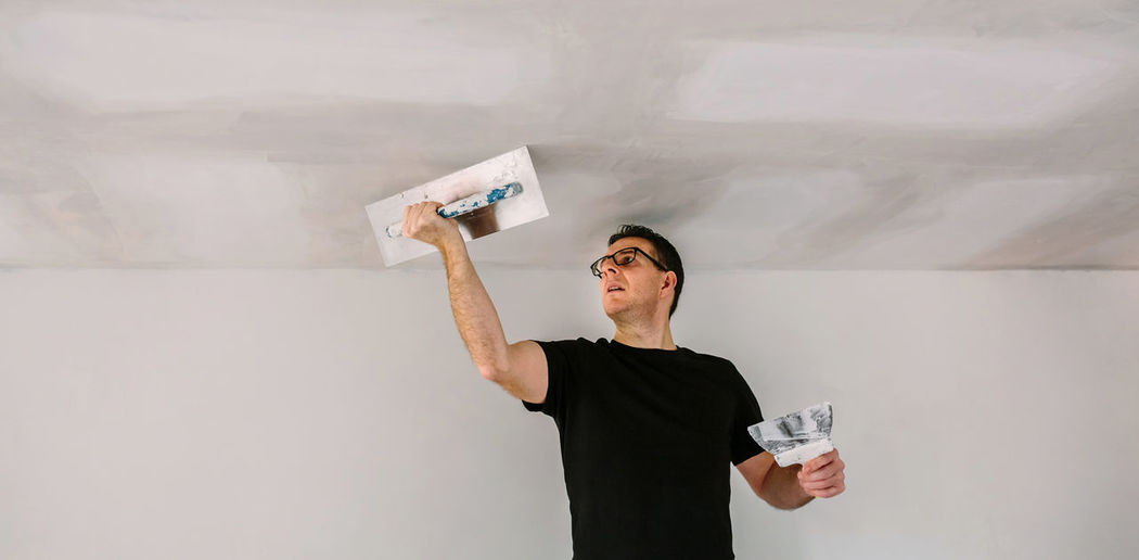 Man plastering ceiling while standing against wall