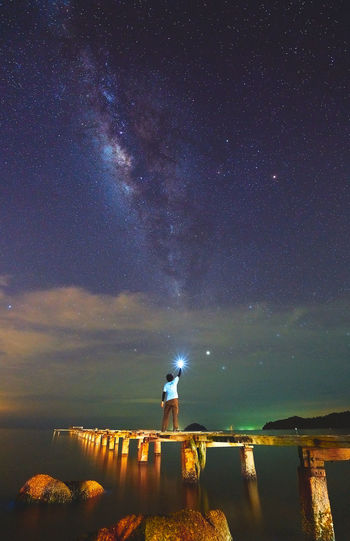 Man holding flashlight while standing on pier over sea against sky at night