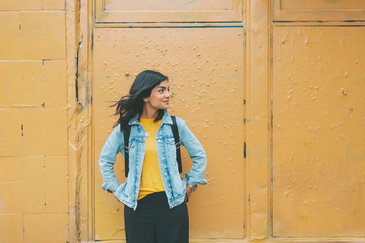 Young woman standing against yellow wall