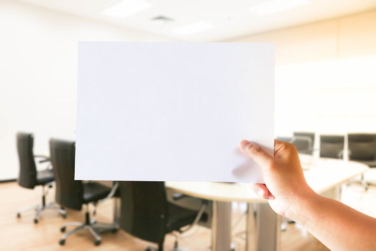 Cropped hand of business person holding blank paper in conference room