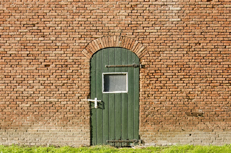 Old brick wall of a farm shed with a green wooden door