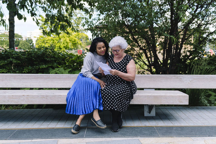 Mother reading letter with daughter sitting on bench at park