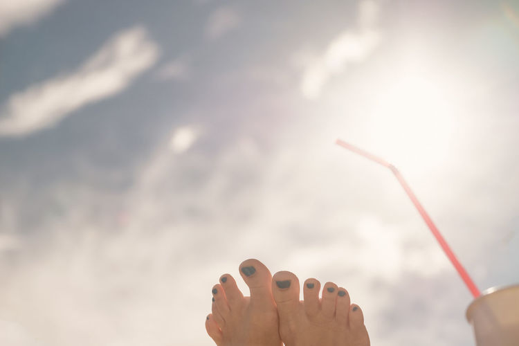 A woman's foot and a drinking straw against cloudy sky