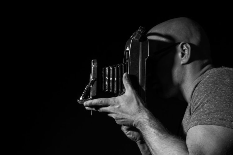 Side view of man photographing with vintage camera against black background