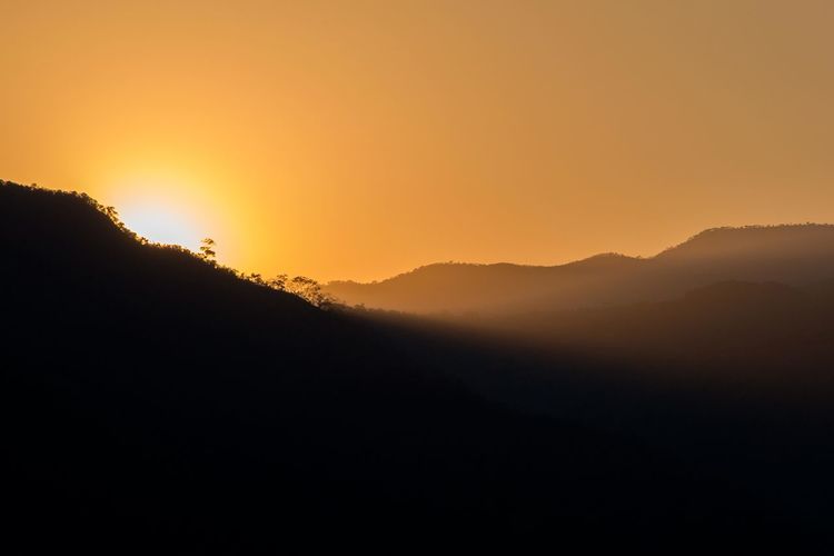 Scenic view of silhouette mountains against orange sky