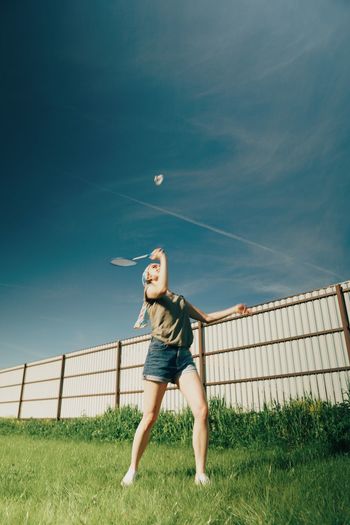 Full length of woman playing badminton on field against sky