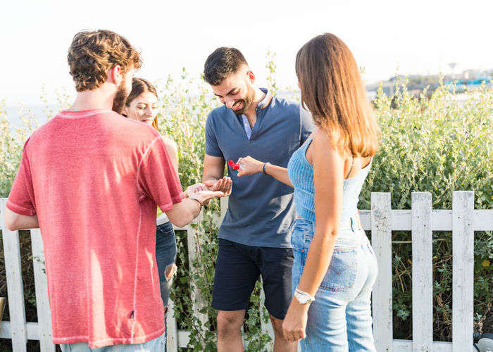 Smiling friends using hand sanitizer outdoors