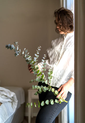 Woman standing by potted plant at home