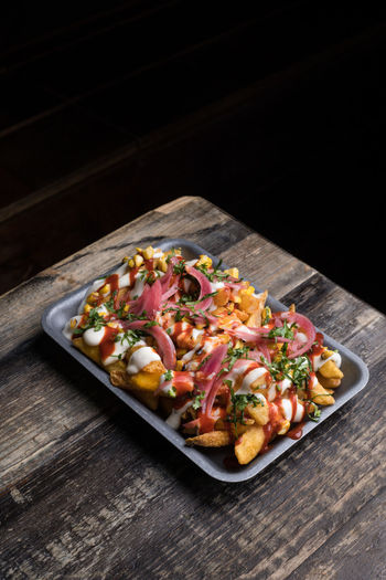 From above of baking tray with appetizing fried potatoes served with sauces placed on wooden table in restaurant