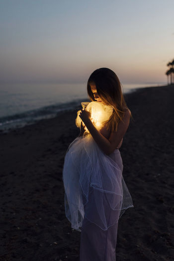 Young woman holding ball of cloth with light at beach