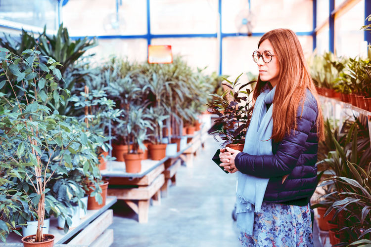 Woman looking away while standing at greenhouse