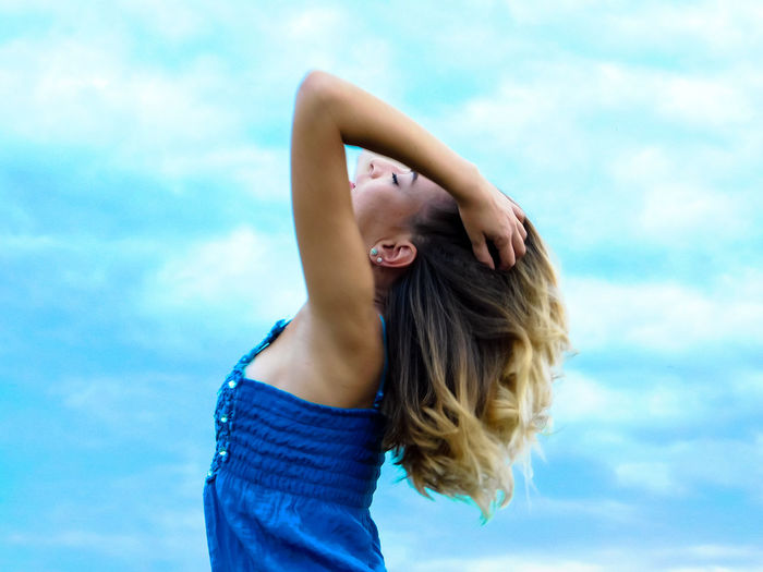 Side view of young woman with hands in hair against sky