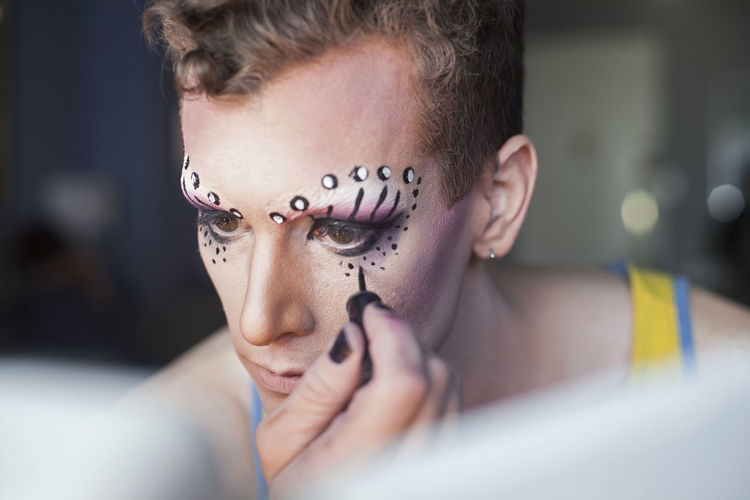 Young man applying drag queen cosmetics