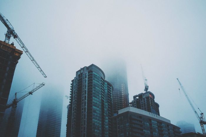 Low angle view of buildings in city against sky during foggy weather