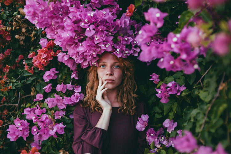 Portrait of beautiful young woman standing by pink flowering plants