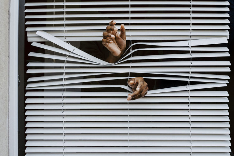 Young man's hands out of window blinds