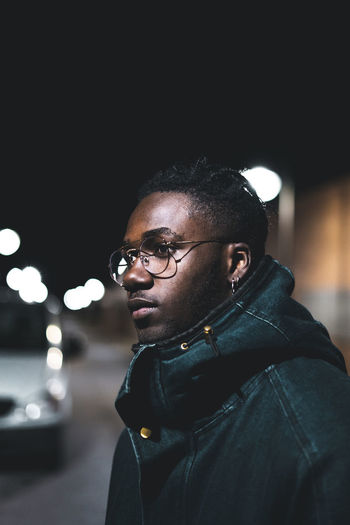 Portrait of young man standing against illuminated wall at night