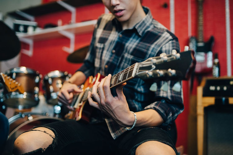 Midsection of man playing guitar while sitting in recording studio