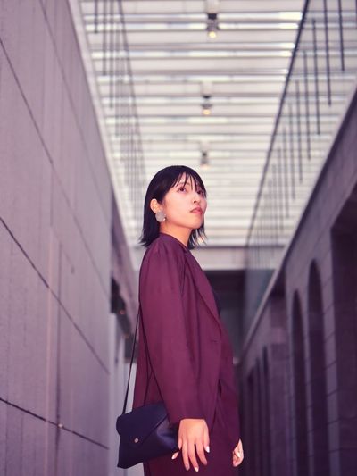 Side view of young woman looking away against building