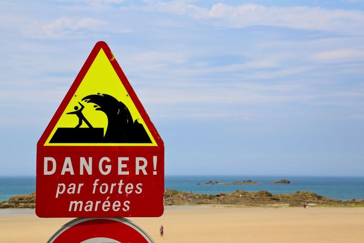 Close-up of danger signboard against the sea