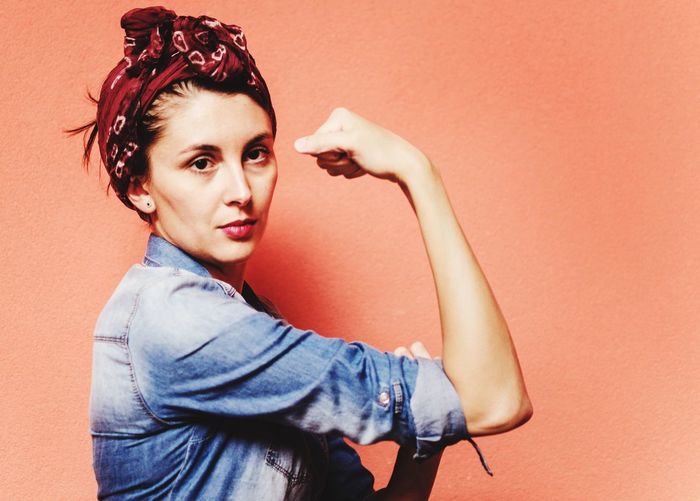 Portrait of beautiful woman flexing muscles against orange wall