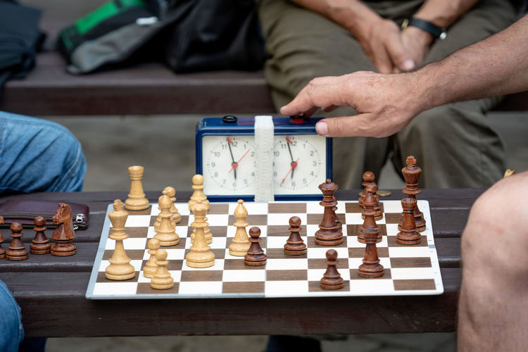 Midsection of men pressing button on clock while playing chess on board