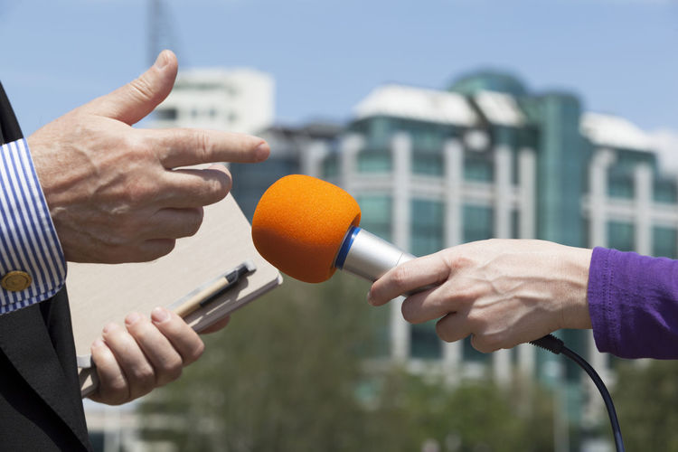 Cropped hand of female journalist interviewing politician in city