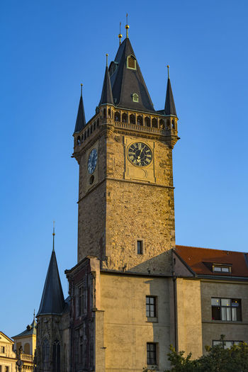 Low angle view of clock tower amidst buildings against clear blue sky