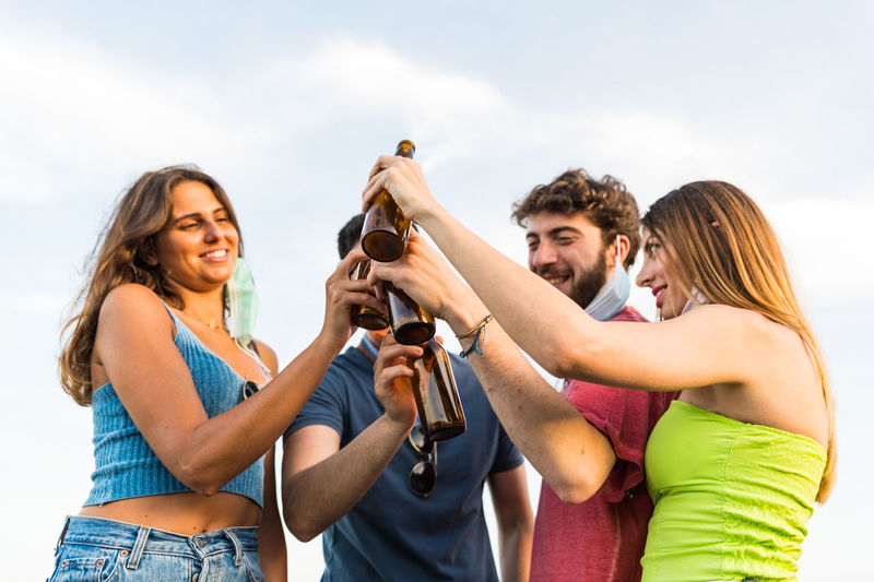 Smiling couple holding beer standing against sky