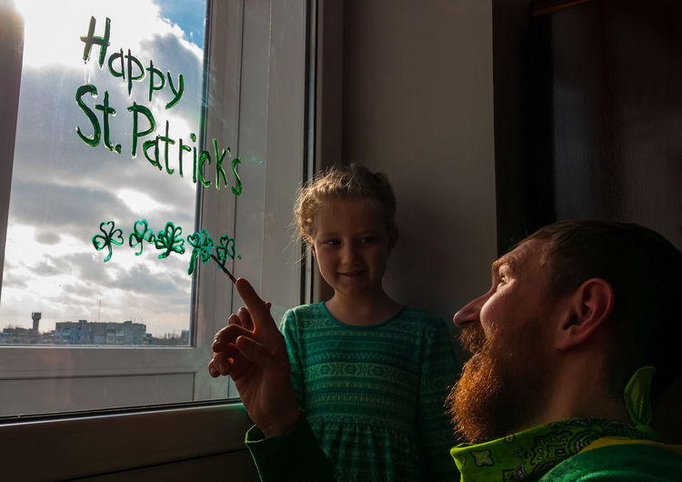 Girl writing on window with father at home