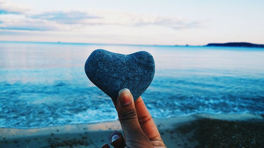 Cropped image of person holding heart shape stone at beach