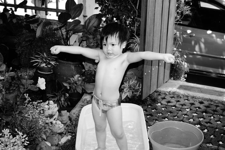 Shirtless boy with arms outstretched standing in bathtub at yard