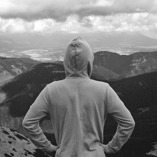 A boy in a sweatshirt from behind on top of a hill enjoys the view in black and white