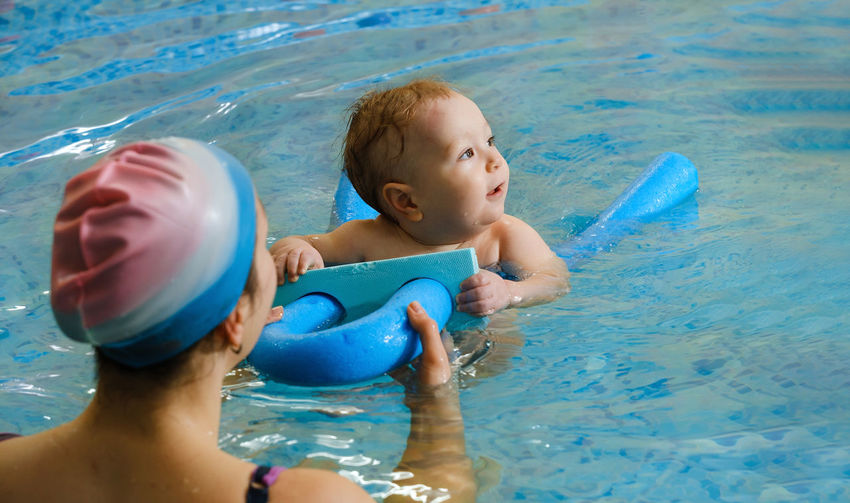 Early age swimming in pool. baby boy trained to swim in water. happy child with trainer woman in