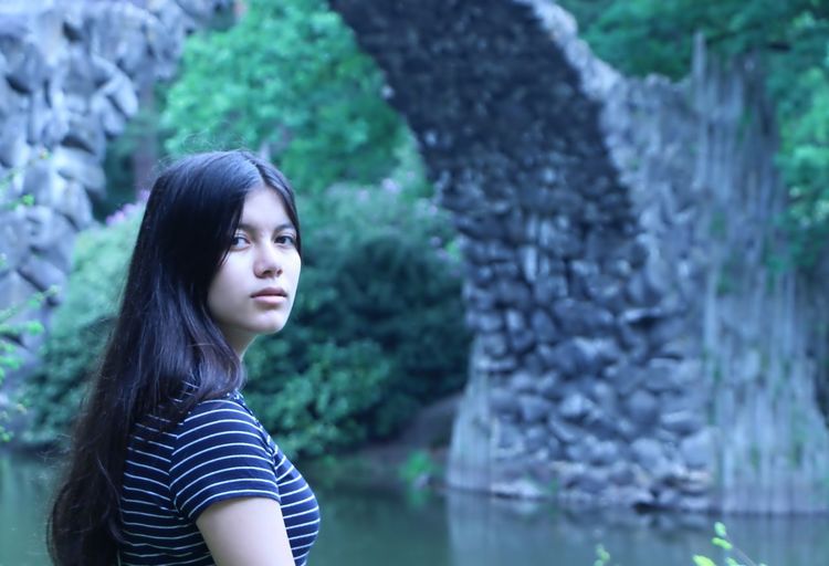 Portrait of young woman standing against rakotzbrucke over river