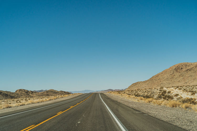 Empty road along landscape against clear blue sky