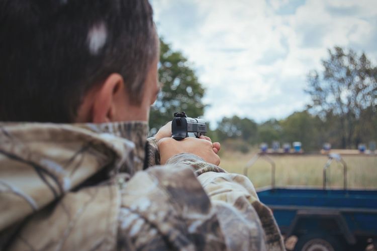 Cropped image of man aiming with gun at shooting range