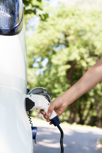 Cropped hand of woman charging electric car at station