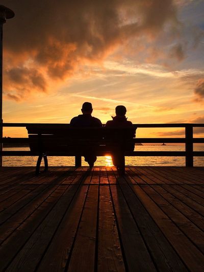 Silhouette people sitting on bench against sky during sunset