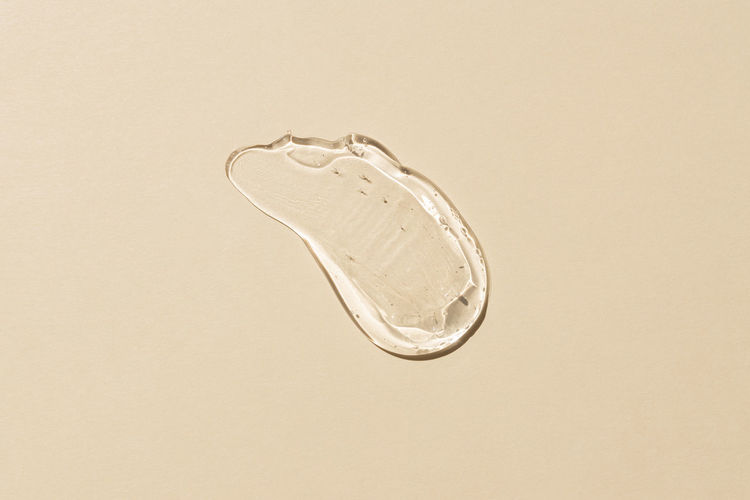 Squeezed cosmetic clear cream gel texture iisolated on beige background. close up transparent serum 