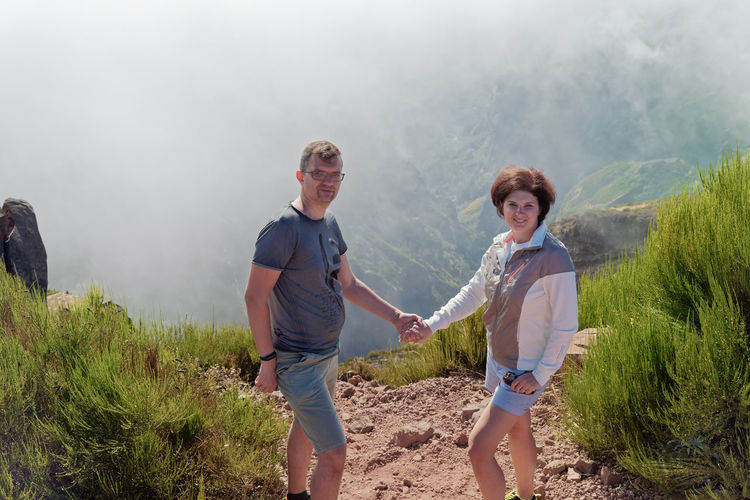 Portrait of couple holding hands standing on mountain during foggy weather