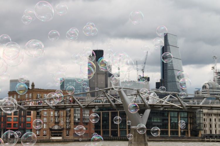 Bubbles blowing against london millennium footbridge and buildings in city 