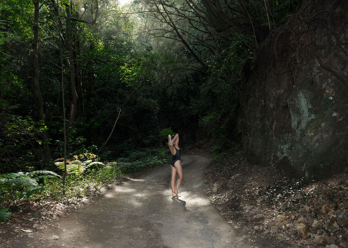 Woman wearing bodysuit standing on road amidst trees in forest