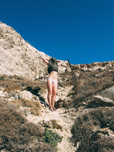 Low angle view of woman removing clothes on mountain against clear blue sky