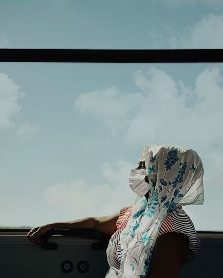 Woman sitting by car against sky