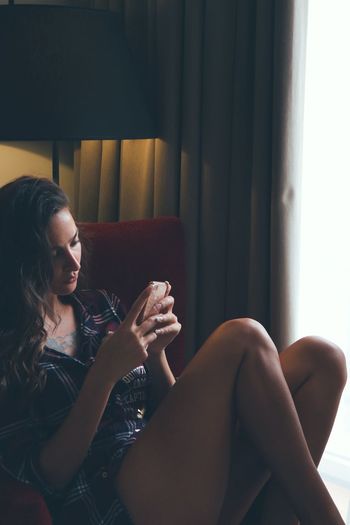 Beautiful young woman using mobile phone while sitting at home