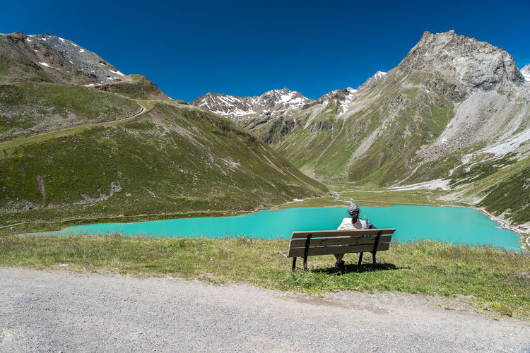 Rear view of woman sitting on bench against lake and mountains