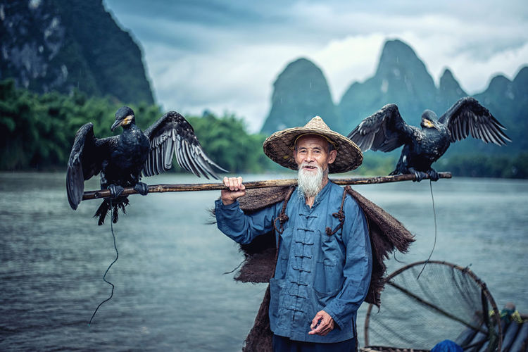 Birds perching on stick held by man in lake

